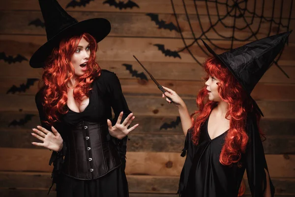 Хэллоуин Концепция - маленькая рыжая ведьма волосы с помощью магии с волшебной палочкой для ее матери с шокированным выражением . — стоковое фото