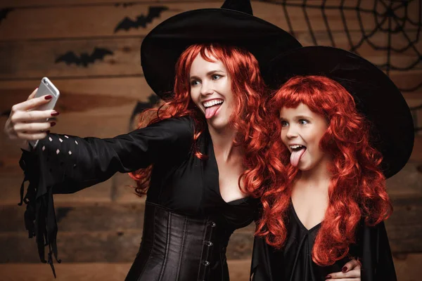 Koncepcja Halloween - piękne kaukaski matka i jej córka z długimi rudymi włosami w stroje czarownic biorąc selfie z smartphone gotowy do odprawiania Halloween. — Zdjęcie stockowe