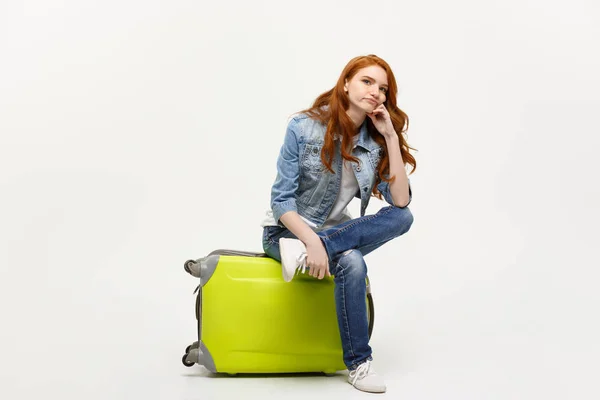 Reise- und Lifestylekonzept - Porträt junge Frau mit rotem Haar sitzt auf einer Tasche mit langweiligem Gesichtsausdruck, isoliert auf leuchtend gelbem Hintergrund. — Stockfoto