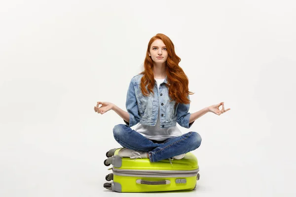 Reisekonzept. junge hübsche Ingwerfrau, die in Lotus-Pose auf dem Gepäckband meditiert. isoliert auf weiß. — Stockfoto