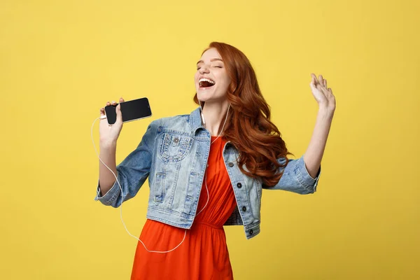 Lifestyle and Music Concept: Beautiful young curly red hair woman in headphones listening to music and dancing on vivid yellow background — Stock Photo, Image