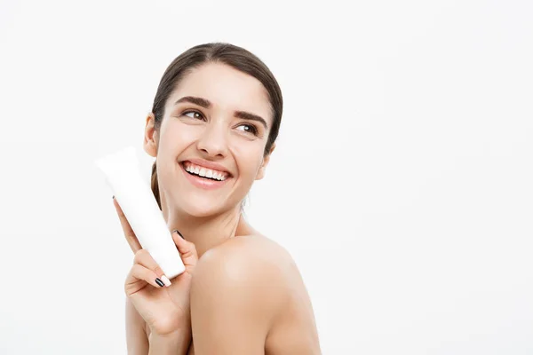 Beauty Youth Skin Care Concept - Beautiful Caucasian Woman Face Portrait holding and presenting cream tube product. Beautiful Spa model Girl with Perfect Fresh Clean Skin over white background.