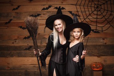 Cadılar Bayramı kavramı - neşeli anne ve kızı cadı kostümleri Cadılar Bayramı ile eğri kabaklar yarasalar ve örümcek ağı ahşap studio arka plan üzerinde poz kutluyor.