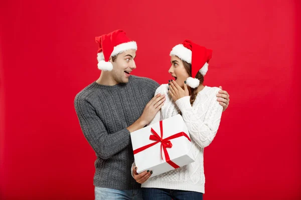 Conceito de Natal - Jovem mulher cobrindo homens olhos com a mão e dando surpresa grande presente. Isolado em fundo vermelho — Fotografia de Stock