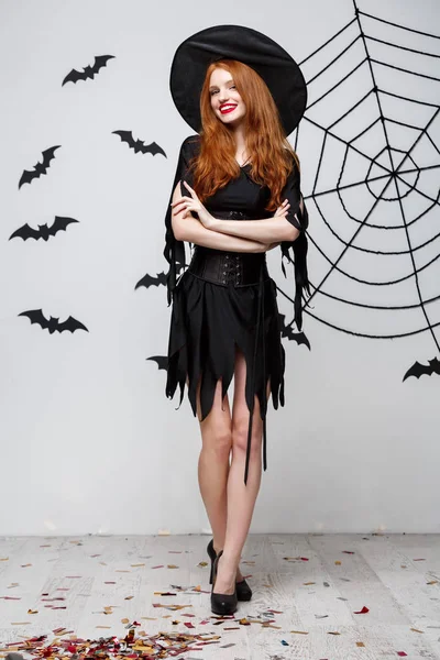 Halloween heks concept - Full-length van Happy Halloween heks holding poseren op donkere grijze studio achtergrond met vleermuis en spider web. — Stockfoto