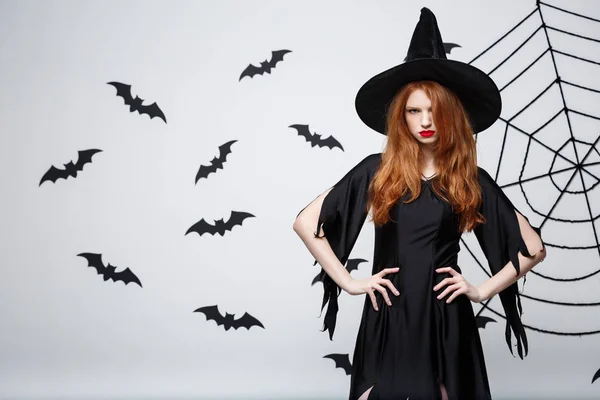 Halloween heks concept - Halloween heks holding poseren met ernstige expressie op donkere grijze studio achtergrond met vleermuis en spider web. — Stockfoto