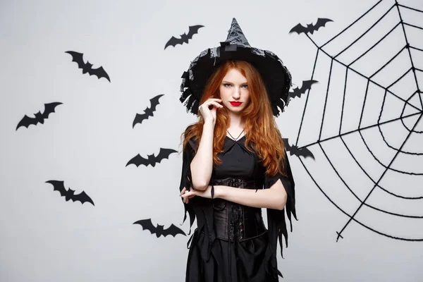 Halloween heks concept - Halloween heks holding poseren met ernstige expressie op donkere grijze studio achtergrond met vleermuis en spider web. — Stockfoto