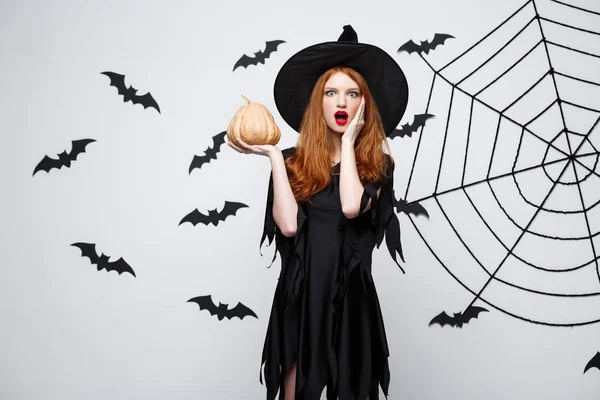 Retrato de una hermosa bruja caucásica sosteniendo calabaza para celebrar Halloween . — Foto de Stock