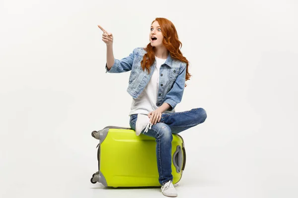 Reise- und Lifestylekonzept: junge kaukasische Frau sitzt auf einem Koffer und weist Richtung. — Stockfoto