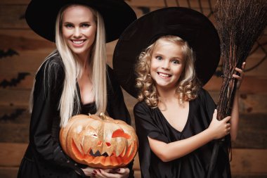 Cadılar Bayramı kavramı - Closeup güzel beyaz anne ve kızı cadı kostümleri Cadılar Bayramı ile eğri kabaklar yarasalar ve örümcek ağı ahşap studio arka plan üzerinde poz kutluyor.