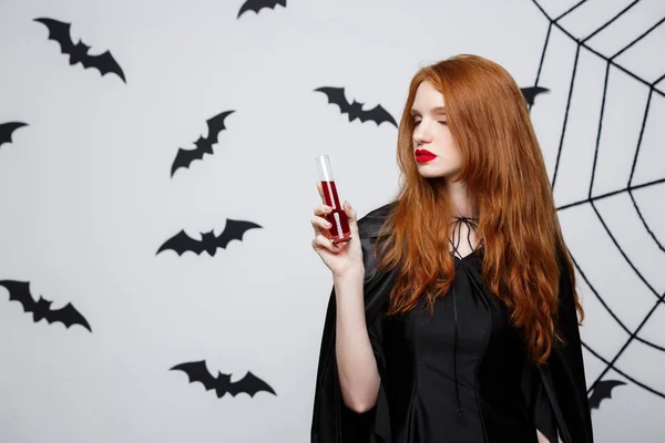 Halloween heks concept - Happy Halloween heks bloed drinken op donkere grijze studio achtergrond met vleermuis en spider web. — Stockfoto