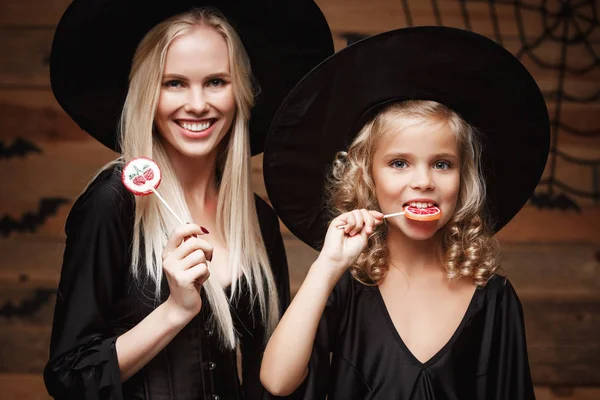 Хеллоуїн концепції - кавказька гарні мати і її дочка відьма костюми святкування Хеллоуїна з Halloween цукерки і солодкий за кажанів та веб-павука на фоні дерев'яні студії. — стокове фото