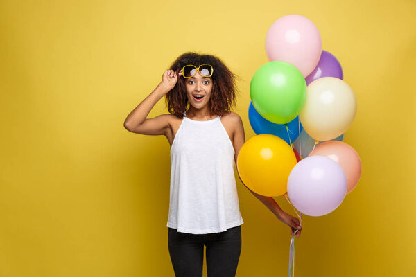Celebration Concept - Close up Portrait happy young beautiful african woman with white t-shirt surprising expression with colorful party balloon. Yellow Pastel studio Background