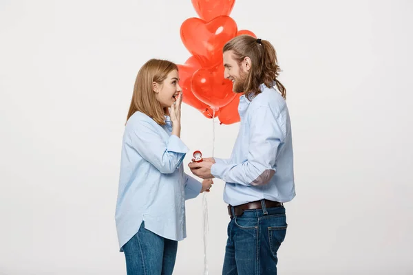 Portret młody przystojny facet daje pierścień z dziewczyną na białym tle z czerwonym sercem balonów. — Zdjęcie stockowe
