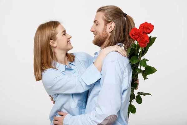 Retrato de un joven atractivo escondiendo flores de su novia antes de darle una sorpresa sobre fondo blanco aislado . —  Fotos de Stock