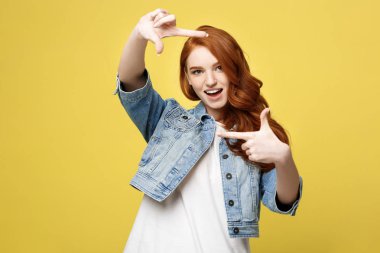 Çilli cheerfuly parmak ile kamera çerçeve yapma gülümseyen güzel zencefil Bayan portresi. Sarı arka plan üzerinde izole. Kopya alanı.