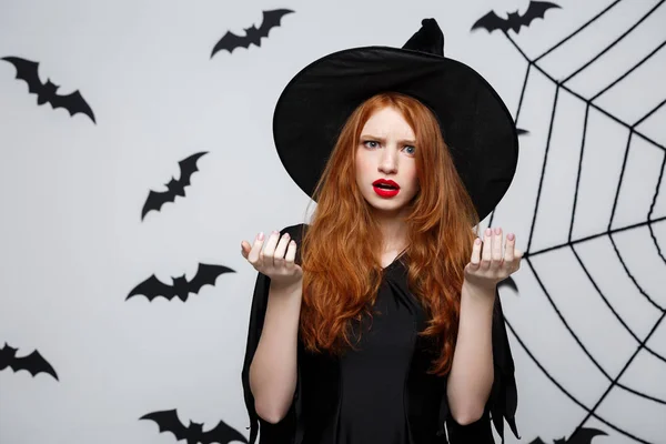 Halloween koncepció - gyönyörű kaukázusi boszorkány sokkoló valami felett szürke háttér. — Stock Fotó