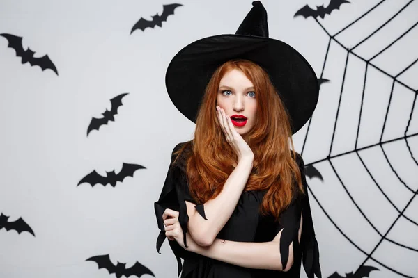 Halloween Concept - mooie Kaukasische heks schokkend met iets over de grijze achtergrond. — Stockfoto