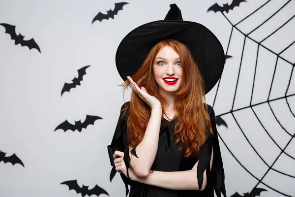 Halloween koncepció - gyönyörű kaukázusi boszorkány meglepő valami felett szürke háttér. — Stock Fotó