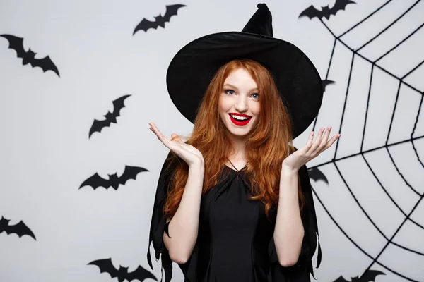 Halloween koncepció - gyönyörű kaukázusi boszorkány meglepő valami felett szürke háttér. — Stock Fotó