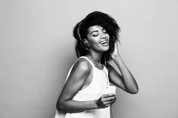Lifestyle Concept - portret van prachtige Afrikaanse Amerikaanse vrouw vreugdevolle luisteren naar muziek op de mobiele telefoon. Geel pastel studio achtergrond. Zwart-wit. — Stockfoto