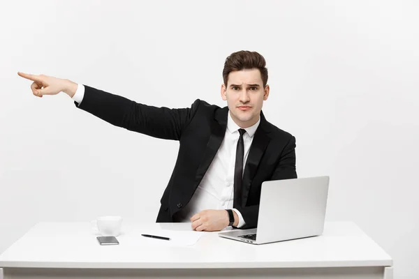 ビジネスコンセプト:スーツを着たハンサムなビジネスマンの肖像は、灰色の背景に隔離されたコピースペースとラップトップで指を指してオフィスに座っています — ストック写真