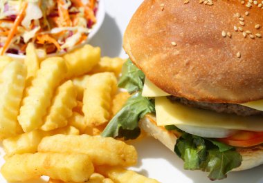 Sığır eti, peynir ve patates kızartması ve salata ofsayt beyaz tabakta sebze ile hamburger. Closeup kopya alanı ile.