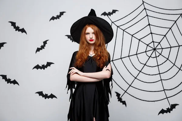 Halloween heks concept - Halloween heks holding poseren met ernstige expressie op donkere grijze studio achtergrond met vleermuis en spider web. — Stockfoto