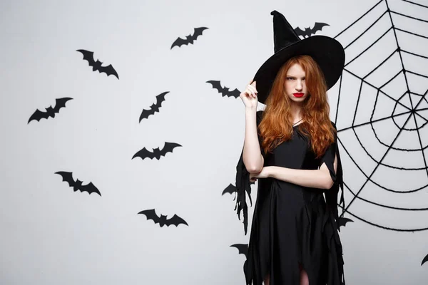 Halloween heks concept - Halloween heks holding poseren met ernstige expressie op donkere grijze studio achtergrond met vleermuis en spider web. — Stockfoto