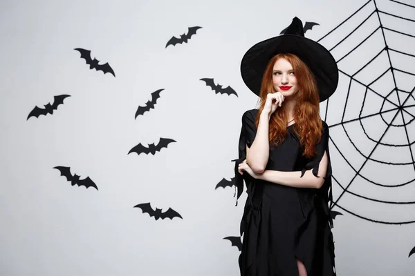 Concepto de bruja de Halloween - Feliz bruja de Halloween posando sobre fondo de estudio gris oscuro con tela de murciélago y araña . — Foto de Stock