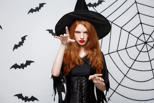 Halloween boszorkány koncepció - Full-length Halloween boszorkány varázslatait, komoly kifejezés alatt sötét szürke stúdió háttere, a denevér és a spider web. — Stock Fotó