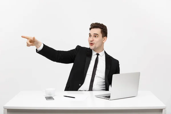 Business Concept: Portret van knappe zakenman gekleed in pak zittend in kantoor wijzend vinger naar kopieerruimte en laptop geïsoleerd over grijze achtergrond — Stockfoto