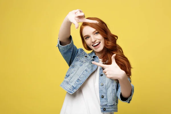 Portrait of young beautiful ginger woman with freckles cheerfuly smiling making a camera frame with fingers. Isolated on yellow background. Copy space. — Stock Photo, Image