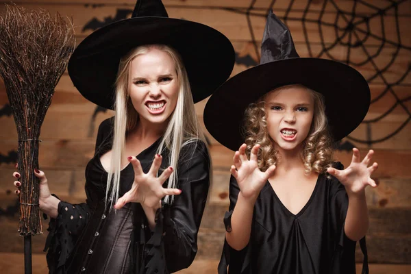 Halloween Concept - Primo piano bella madre caucasica e sua figlia in costumi da strega che celebrano Halloween in posa con zucche curve su pipistrelli e ragnatela su sfondo studio di legno . — Foto Stock