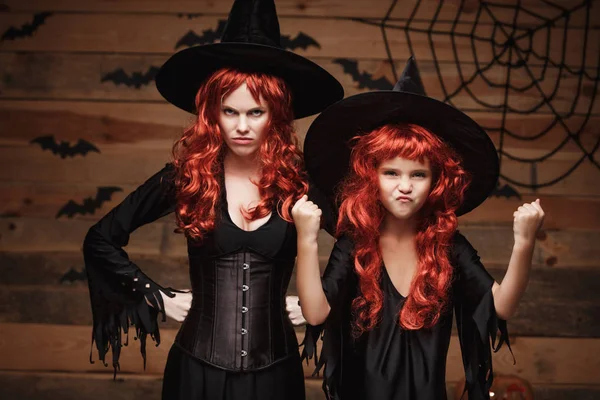 Halloween Concept - mooie Kaukasische moeder en haar dochter met lange rode haren in heks kostuums heks vrolijke vechten gelaatsuitdrukking. — Stockfoto