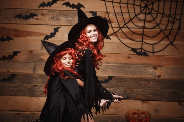 Хэллоуин - мать и ее дочь с длинными рыжими волосами в париках летают волшебной метлой . — стоковое фото