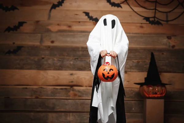 Koncepcja Halloween - mały biały Duch halloween dynia cukierki jar robi Cukierek albo psikus z zakrzywione dynie przez nietoperze i pajęczyna na podłoże drewniane studio. — Zdjęcie stockowe