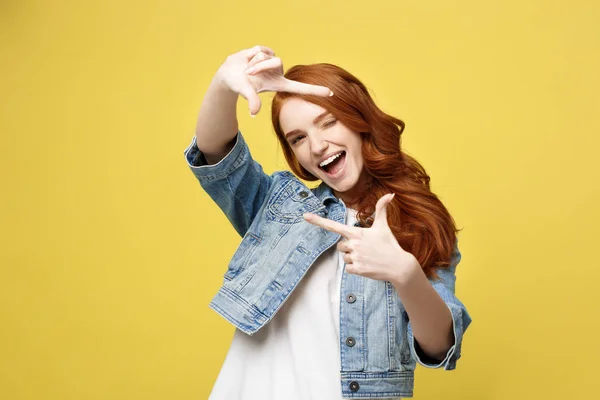 Retrato de una joven hermosa pelirroja con pecas sonriendo alegremente haciendo un marco de cámara con los dedos. Aislado sobre fondo amarillo. Copiar espacio . —  Fotos de Stock