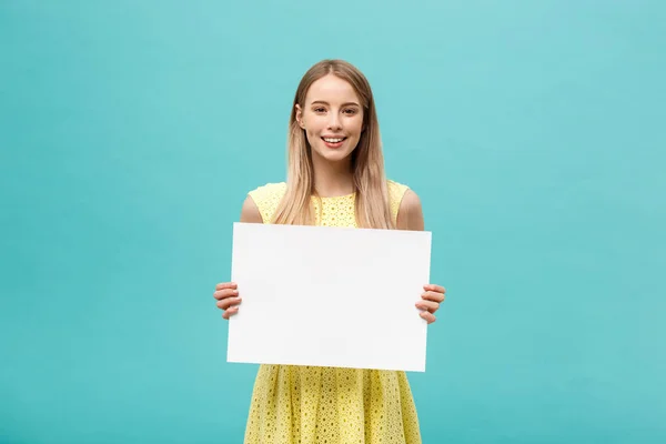 Lifestyle Concept: young beautiful girl smiling and holding a blank sheet of paper, dressed in yellow, isolated on pastel blue background — Stock Photo, Image