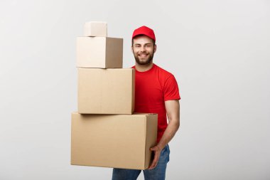 Teslimat kavramı: Yakışıklı teslimat adam tutun kazık karton kutular gri arka plan üzerinde.