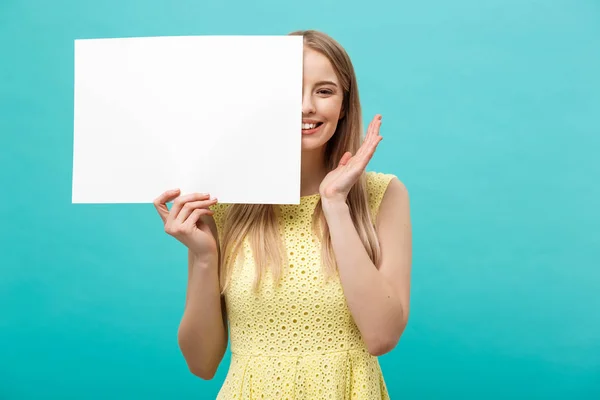 Lifestyle Concept: young beautiful girl smiling and holding a blank sheet of paper, dressed in yellow, isolated on pastel blue background — Stock Photo, Image
