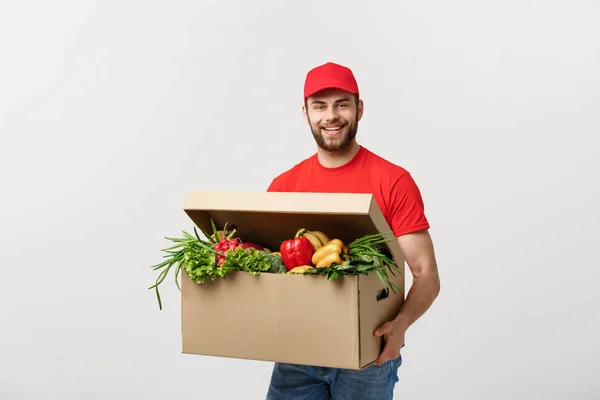 Концепция поставки: Привлекательный кавказский курьер в красной форме с коробкой со свежими фруктами и овощами — стоковое фото
