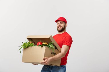 Teslimat kavramı - yakışıklı Cacasian teslimatçı bakkal yiyecek ve içecek deposundan paket kutu taşıyan. Arka plan gri studio izole. Kopya alanı.