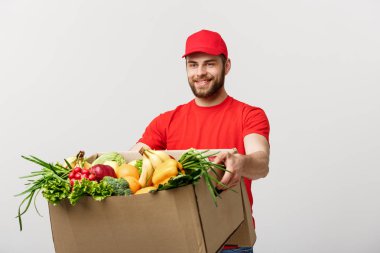 Teslimat kavramı - yakışıklı Cacasian teslimatçı bakkal yiyecek ve içecek deposundan paket kutu taşıyan. Arka plan gri studio izole. Kopya alanı.