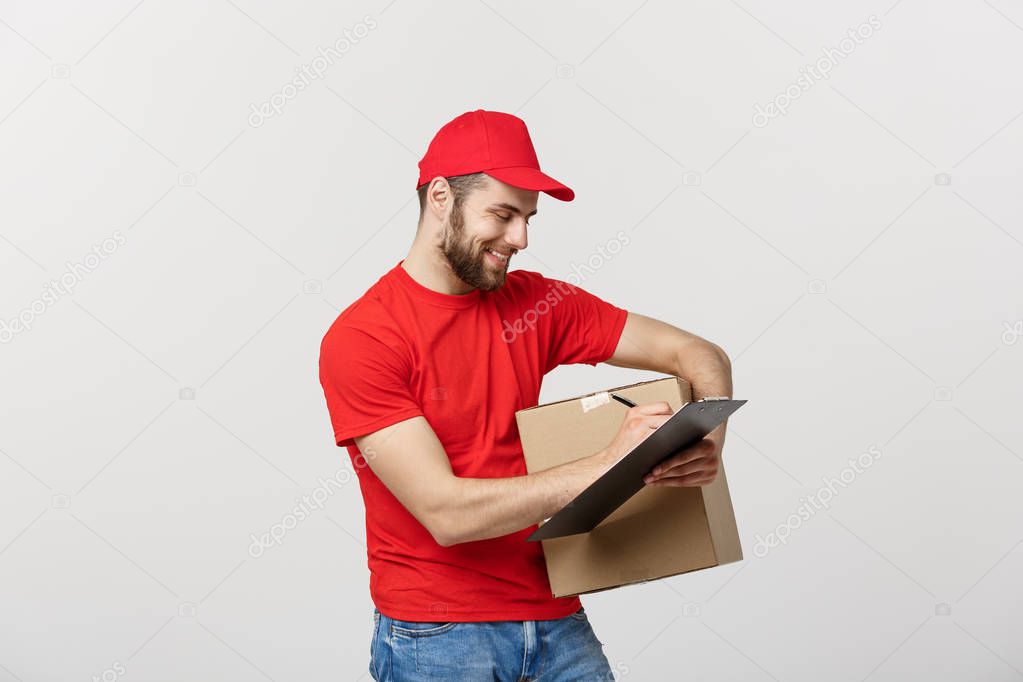 Portrait of smiling male delivery man writing on clipboard and holding box. Isolated over white background