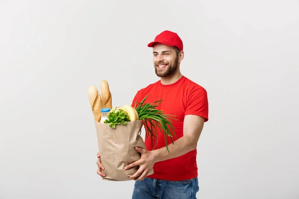 Conceito de entrega - Bonito homem de entrega Cacasian transportando saco de embalagem de comida e bebida de supermercado da loja. Isolado no estúdio Grey Background. Espaço de cópia . — Fotografia de Stock