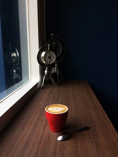 Czerwony kubek kawy cappuccino w czasie rano, z tle zegar vintage. — Zdjęcie stockowe