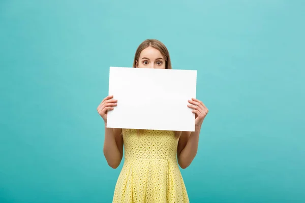 Retrato de close-up, jovem mulher em vestido amarelo segurando papel liso branco com expressão chocada no que ela vê, fundo azul isolado . — Fotografia de Stock