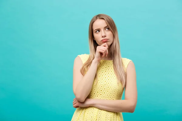 Denken vertrouwen jongedame in gele jurk opzoeken van geïsoleerde op blauwe achtergrond — Stockfoto
