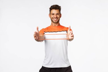 Yakışıklı genç sporcu, fitness eğitmeni antrenman sırasında ne kadar kolay direnç bandı kullandığını, kaygısız ve hevesli gülümsediğini gösteriyor. Erkek sporcu spor aletleri kullanıyor.